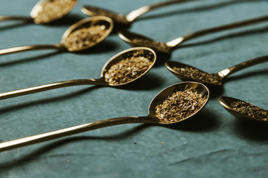 Loose tea leaves on golden spoons in close-up.